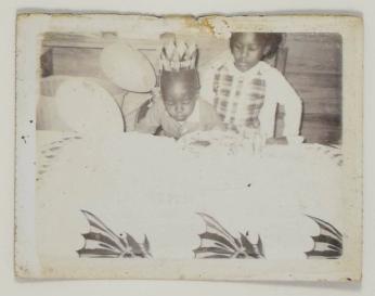 [Young Child in Birthday Hat Blowing out Candles, Young Girl Behind Them]