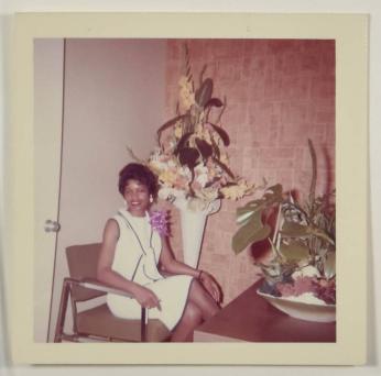 [Woman Smiling, Seated in Front of Flower Arrangement, Wearing Corsage]