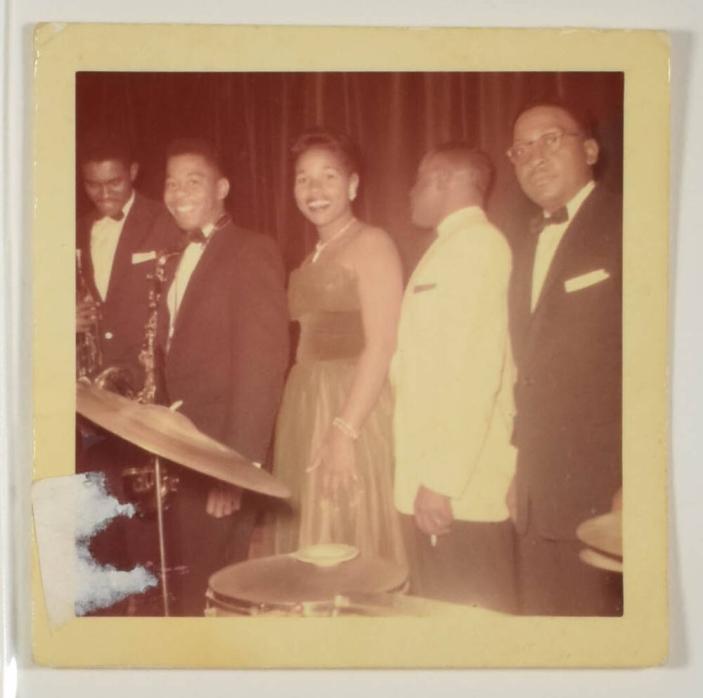 [Woman in Dress Smiling with Musicians Holding Saxophones]