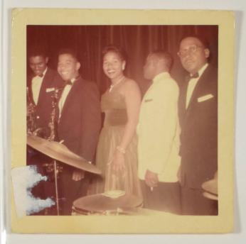 [Woman in Dress Smiling with Musicians Holding Saxophones]