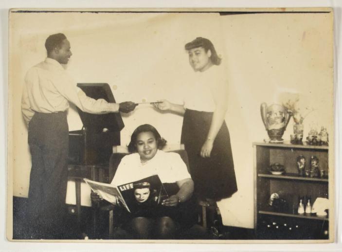 [Woman Seated in Chair Reading Life Magazine, Behind Her a Woman Passing a Man a Record to Play]