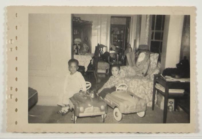 [Two Young Kids Posed in Living Room with Toy Cars]