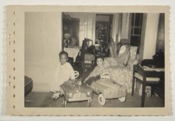 [Two Young Kids Posed in Living Room with Toy Cars]