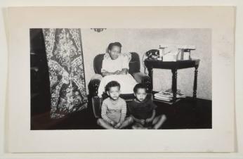 [Woman Seated in Chair with Two Young Children Seated on Floor in Front]