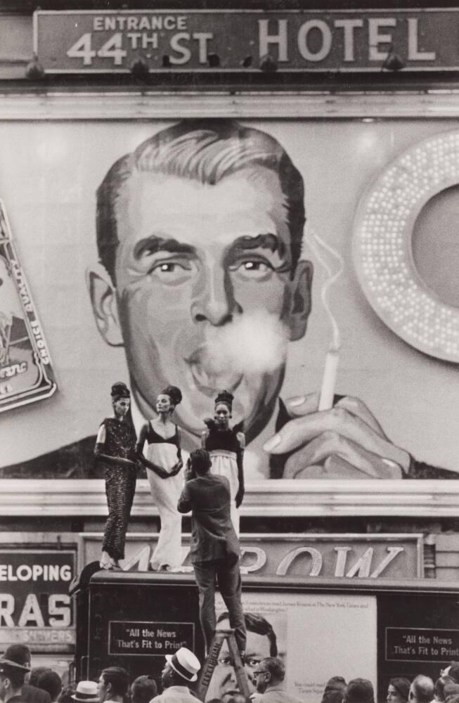 [Three Models Being Photographed in Front of ‘44th St Hotel’ Image of Man Blowing Smoke]