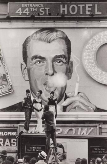 [Three Models Being Photographed in Front of ‘44th St Hotel’ Image of Man Blowing Smoke]