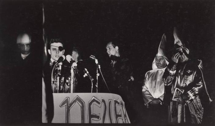 [Man With Eye Patch at Microphone Flanked by Two Kkk Members, American Flag  Sign ‘Never Say Tomorrow']