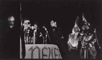 [Man With Eye Patch at Microphone Flanked by Two Kkk Members, American Flag  Sign ‘Never Say Tomorrow']