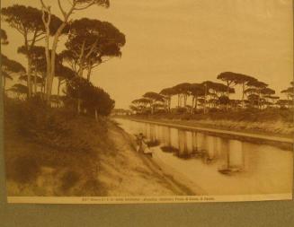 Canal.  Two figures seated along left bank. Top "tufted" tall pine trees on either side.