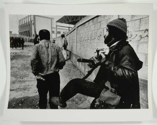 A Christian Phalangist soldier kicks a Palestinian along a bullet-riddled factory wall